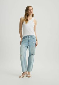 Jeans desgastados de color azul claro con adornos de perlas, combinados con una camiseta de tirantes blanca de canalé y sandalias de tacón alto blancas.
