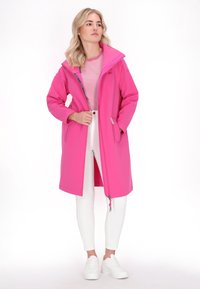 Rožinė ilga striukė, pagaminta iš lygios medžiagos, su gobtuvu, užtrauktukais priekinėse kišenėse ir tiesia forma. Derinama su juostuotu marškinėliu ir baltomis kelnėmis.