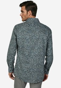 Overhemd met lange mouwen in donkerblauwe stof met een dicht bloemenpatroon in lichtblauw en geel. Standaardkraag en afgeronde zoom.