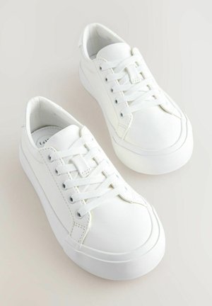 Un paio di sneaker bianche low-top con lacci bianchi e suole in gomma spessa su uno sfondo chiaro.