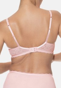 Różowy koronkowy stanik z regulowanymi ramiączkami i zapięciem na haczyk. Posiada falbaniasty brzeg i gładką teksturę. Widok z tyłu jest widoczny.