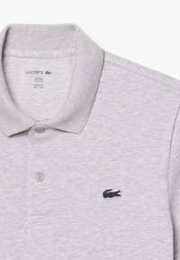 Polo gris de algodón con un acabado texturizado. Presenta un cuello clásico, dos botones y un pequeño logo de cocodrilo bordado en negro.