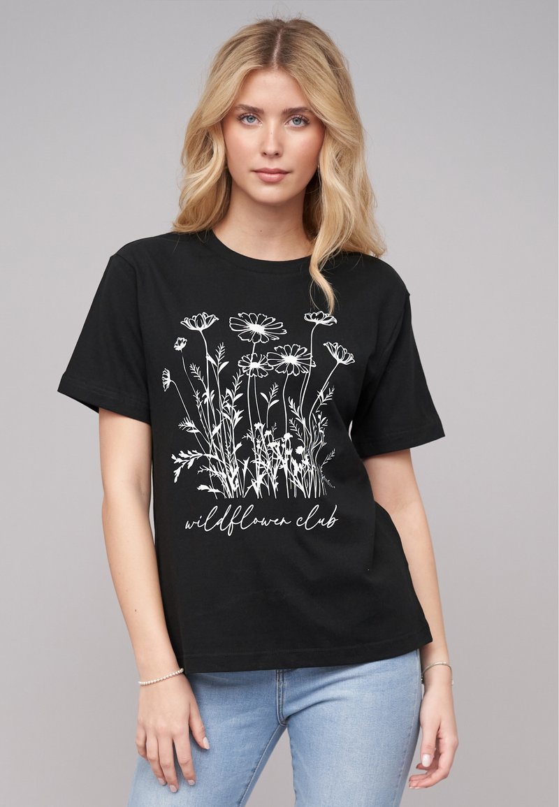 T-shirt en coton noir avec une illustration botanique blanche de fleurs et le texte "club des fleurs sauvages" en police cursive. Manches courtes.