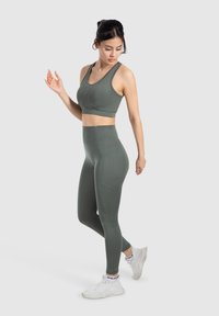 Conjunto atlético en verde oliva que incluye un top corto ajustado y mallas de cintura alta, fabricado con un material suave y elástico con un diseño sin costuras.