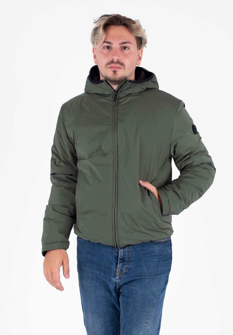 Veste à capuche verte olive avec fermeture éclair, poches latérales et texture lisse. Portée avec un jean en denim bleu.