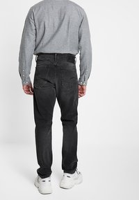 Vaqueros de mezclilla negros con corte recto, que presentan un diseño clásico de cinco bolsillos y textura desgastada. Combinados con una camiseta de manga larga gris y zapatillas blancas.