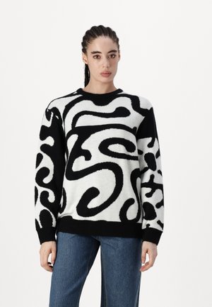 Black and white sweater with a textured, abstract swirl pattern; round neckline, long sleeves, and a ribbed hem. Paired with blue denim pants.