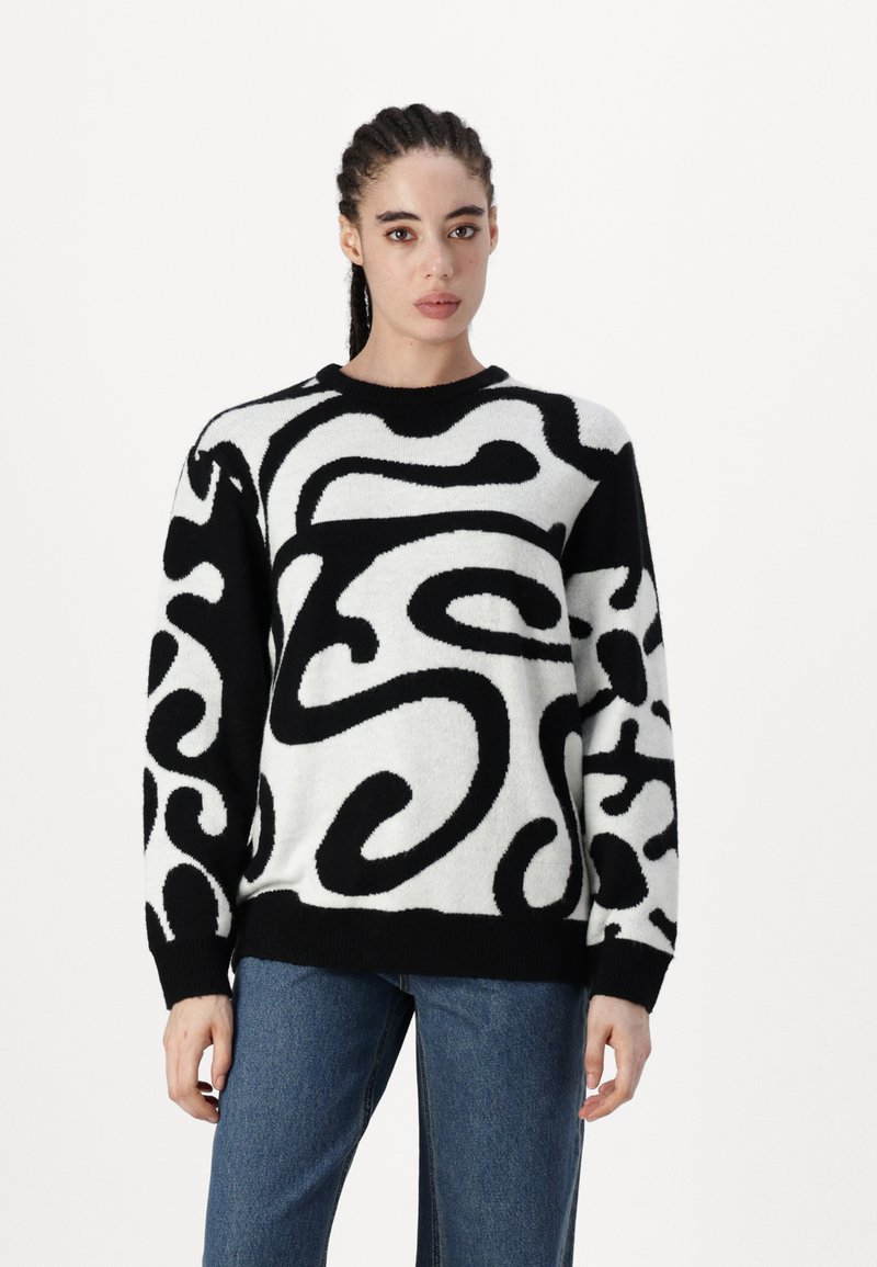 Pull noir et blanc avec un motif texturé en tourbillon abstrait ; encolure ronde, manches longues et ourlet côtelé. Assorti à un pantalon en denim bleu.