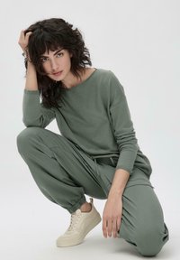 Chemise à manches longues vert clair et pantalon large assorti en tissu doux, associés à des baskets crème. Design simple et décontracté, poignets élastiques.