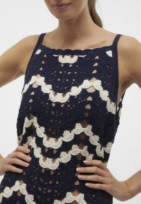 Top all'uncinetto blu navy e crema con un motivo a scallop, trame aperte e spalline sottili. Tessuto testurizzato con colori a contrasto.
