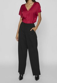 Blusa rossa in satin con scollo a V e maniche corte, abbinata a pantaloni neri a vita alta. Presenta tasche laterali e una vestibilità su misura.