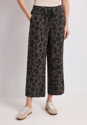 Pantalon court à jambes larges avec imprimé léopard marron foncé et noir, taille élastique avec cordon de serrage, porté avec des baskets beiges.