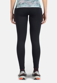 Mustat leggingsit, joissa on sileä rakenne ja tiukka muotoilu, yhdistettynä harmaisiin ja oransseihin juoksukenkäisiin, nähtynä takaa.