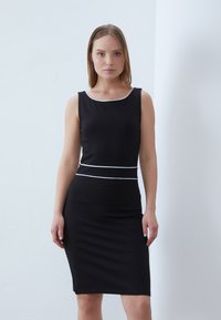 Black sleeveless dress made of stretchy fabric, featuring a fitted silhouette, white accents along the neckline and waist, and a knee-length cut.