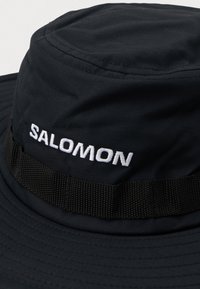 Chapéu de balde preto com aba larga cosida e faixa preta, apresentando o logótipo "SALOMON" bordado em branco à frente.