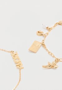 Deux bracelets à breloques en or sur une surface blanche, l'un avec le texte "AMORE", l'autre avec une plaque rectangulaire, des lèvres, une perle et des breloques de chérubin.