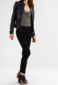 Zwarte leren jas over een grijs gerimpeld topje, gecombineerd met zwarte skinny jeans en open teen zwarte hoge hakken met tan accenten.