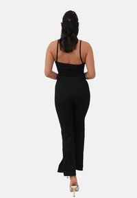 Combinaison noire avec un bustier ajusté et des jambes évasées. Dotée de fines bretelles spaghetti et d'un tissu texturé. Portée avec des chaussures à talons clairs.
