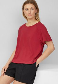 T-shirt rosso a maniche corte in vestibilità relax, realizzato in morbido cotone; presenta un collo rotondo e maniche raglan, abbinato a pantaloni corti neri.