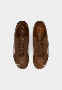 Brune ruskinds-sneakers med hvide detaljer, tekstureret design, rund tå, flade snørebånd, Ortholite-indlægssål og en karakteristisk Puma-logo.