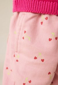 Pantaloni rosa in denim con un bordo a coste rosa, caratterizzati da un motivo ripetuto di ciliegie rosse e verdi.