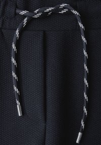 Zwarte, textuurstof heeft een trekkoord met een gevlochten patroon in wit en zwart, en zilveren metalen aglets aan de uiteinden.
