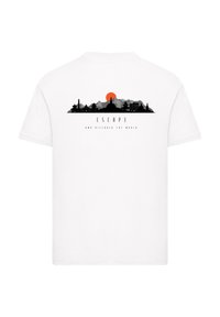 White cotton T-shirt featuring a black skyline graphic with a red sun, and the text "ESCAP3 AND DISCOVER THE WORLD" below.