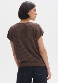 Top in maglia marrone con un motivo texturizzato, maniche corte e vestibilità rilassata, abbinato a jeans in denim scuro.
