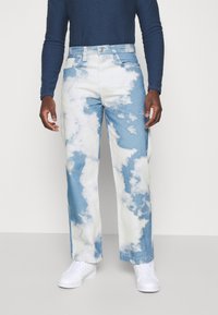 Jeans har ett blått och vitt molnmönster, med en avslappnad passform och raka ben. Materialet är klassisk denim, i kombination med vita sneakers.