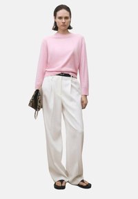 Lichtroze trui, witte wijde broek, zwarte riem en een oversized slangenprint clutch. Zwarte slippers maken de outfit compleet.