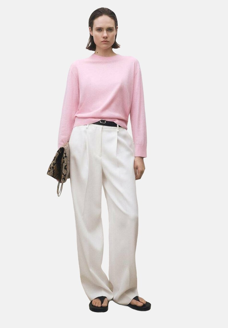 Lichtroze trui, witte wijde broek, zwarte riem en een oversized slangenprint clutch. Zwarte slippers maken de outfit compleet.