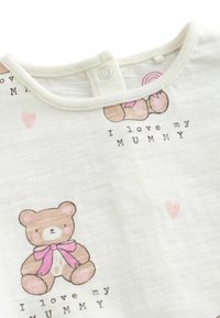 T-shirt en coton blanc avec un col rond, mettant en avant un ours en peluche marron avec un nœud rose et le texte "J'aime ma MAMAN" accompagné de petits cœurs roses.
