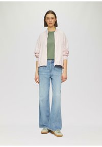 Jasnoróżowa kurtka bomberka na zielonej bluzce, zestawiona z szerokimi niebieskimi dżinsami i beżowymi trampkami. Prosty design z luźnym krojem.