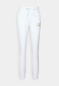 Bílé tepláky vyrobené z měkkého materiálu, se stahovací šňůrkou v pase a žebrovanými manžetami. Na boku je vytištěno logo "Versace Jeans Couture" ve zlaté barvě.