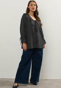 Svart långärmad topp med volanger, snörning i halsen och vida ärmar. Matchad med mörkblå vida jeans och svarta lägenheter.