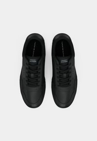 Baskets noires en matériau synthétique à texture lisse, bout rond, lacets plats et logo sur la semelle intérieure. Design simple avec des accents minimaux.