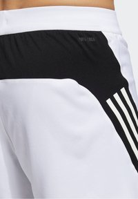 Valkoiset urheilushortsit, joissa on musta joustava vyötärö, musta sivupaneeli ja kolme valkoista pystysuoraa raitaa sivussa.