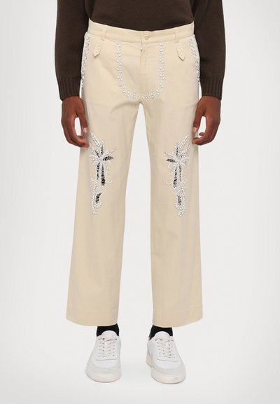 Pantaloni larghi beige con dettagli intricati in ricamo floreale argento e nero, realizzati in una miscela di cotone con una texture liscia.