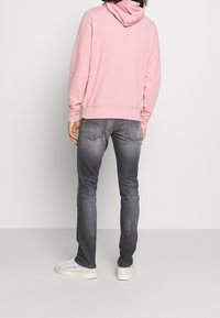 Světle růžová mikina s kapucí, šedé džíny a bílé tenisky. Mikina má stahovací kapuci a žebrované manžety, džíny mají přiléhavý střih.