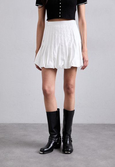 White pleated mini skirt with a fitted waistband and soft texture, paired with black knee-high leather boots featuring silver accents.