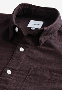 Bordeaux knoopshirt met kraag, met witte knopen en een borstzak. De stof heeft een gestructureerde uitstraling. Etiket leest "NEXT," maat M.