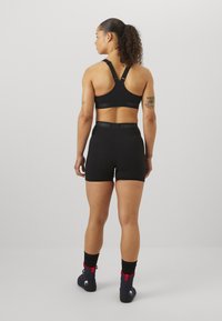 Fekete sportmelltartó versenyháttal és állítható pántokkal, magas derekú fekete sorttal, amelyen Venum logós derékrész található.