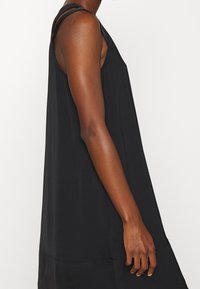 Vestido negro sin mangas con un corte holgado, tejido ligero y una silueta recta. Presenta un escote redondeado y hombros anchos.