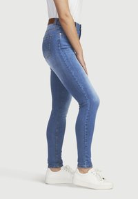 Korkeavyötäröiset siniset farkut, joissa on slim fit -sovitus, valmistettu denimistä. Ominaisuuksiin kuuluvat etu- ja takataskut, kevyt kuluminen ja ruskea nahkahihna.