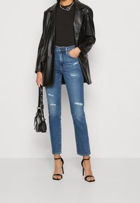 Svart läderblazer, åtsittande svart topp, slitna blå denimjeans och svarta sandaler med remmar. Accessoarer inkluderar en liten svart handväska.