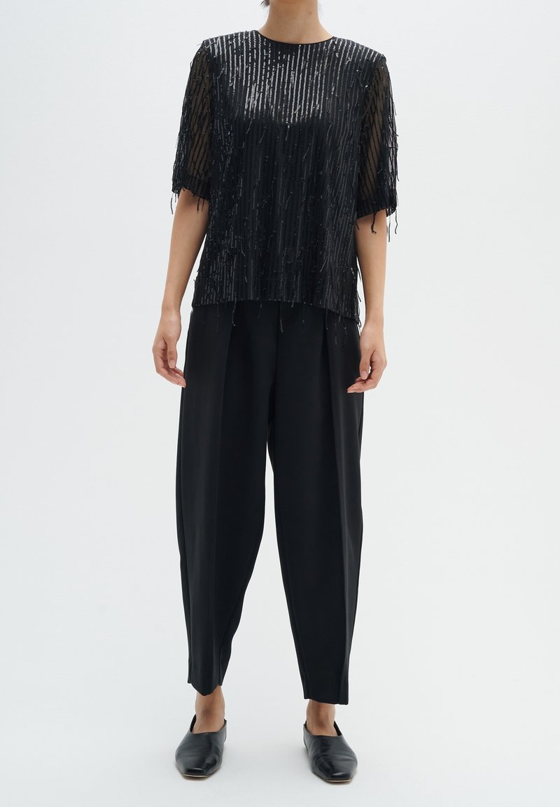 Top nero con paillettes e maniche corte, abbinato a pantaloni neri larghi. Texture liscia, forma rettangolare e dettaglio a frange a strati all'orlo.