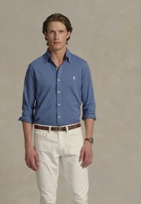 Lichtblauwe lange mouwen overhemden, witte broek, bruine riem en horloge. Eenvoudig ontwerp, klassieke pasvorm, katoenmateriaal en geen zichtbare patronen.