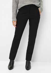 Pantaloni neri su misura realizzati in tessuto morbido con vestibilità dritta. Presentano una chiusura con un solo bottone e tasche laterali. Indossati con stivali alla caviglia.