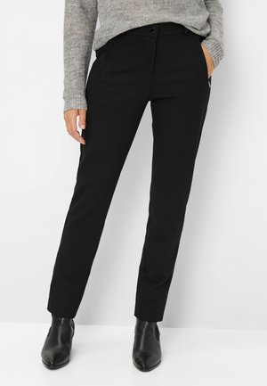 Sorte skræddersyede bukser lavet af glat stof med lige pasform. Har en enkelt knaplukning og sidelommer. Bæres med ankelstøvler.