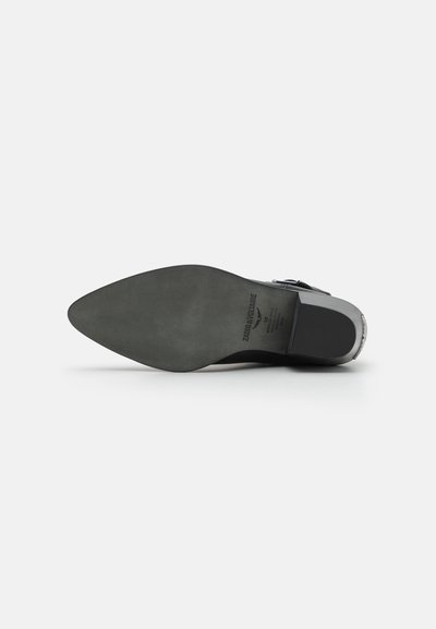 Semelle de chaussure en cuir noir avec une forme pointue, présentant une texture lisse et un branding minimal. Accentué par un talon métallique.